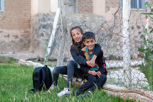 Dos hermanos y hermanas refugiados están sentados junto a una cerca trenzada para niños. photo