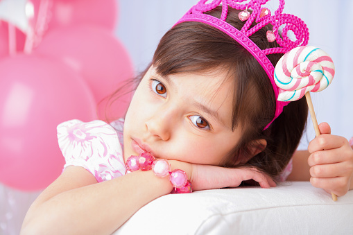 Sulking 8 years girl all dress up celebrating her birthday laying on white couch.