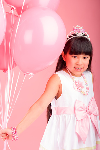 Smiling 8 years old girl celebrating birthday on pink background holding balloons