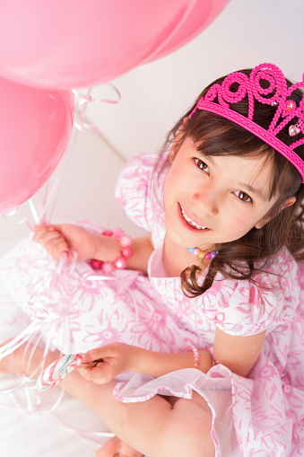 Smiling 8 years girl all dress up celebrating her birthday offering her lollipop sitting on white couch.