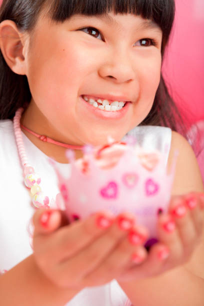 Smiling 8 years old girl celebrating birthday on pink background holding cupcake up close.