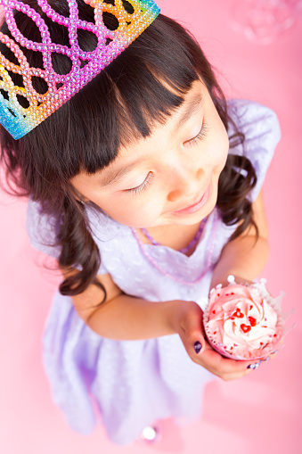 Smiling 7 years old girl celebrating birthday on pink background holding cupcake up close.