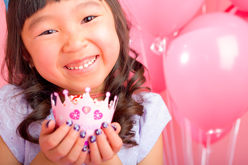 Smiling 7 years old girl celebrating birthday on pink background holding cupcake up close.