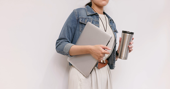 closeup of asian businesswoman wearing jacket holding laptop and reusable eco friendly stainless steel water bottle at office  - coffee in reusable thermo mug