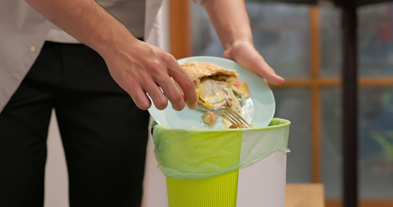 close up of asian man scraping food leftovers or waste into kitchen bucket - Waste separation and environmental friendly in business office