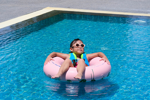 Little girl in a swimsuit relaxing on the inflatable ring in pool. Cute little girl playing in the pool on a sunny day. Summer lifestyle concept.