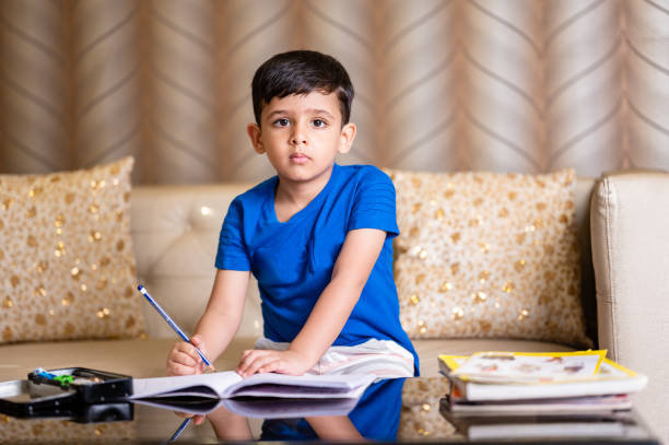 aufnahme eines hart arbeitenden kleinen jungen, der seine schularbeiten zu hause macht - reading and writing little boys reading asian ethnicity stock-fotos und bilder