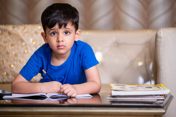 aufnahme eines hart arbeitenden kleinen jungen, der seine schularbeiten zu hause macht - reading and writing little boys reading asian ethnicity stock-fotos und bilder