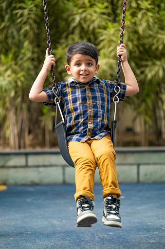 Adorable happy little kid having fun to play swing at the playground.