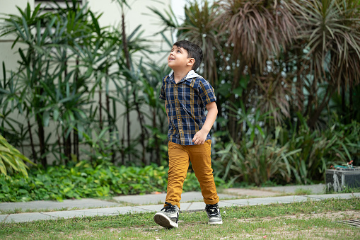 Outdoor Portrait of a happy little boy walking , running and playing games in a public park.