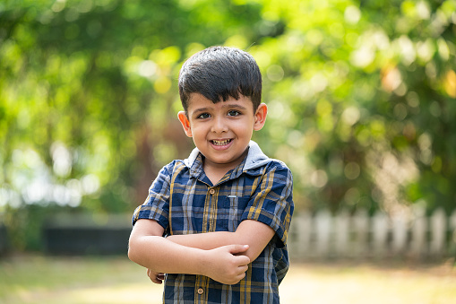 Portrait of happy little boy wearing casual dress laughing outdoor, standing straight in a public park and looking at camera.