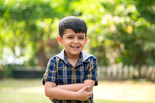 Portrait of happy little boy wearing casual dress laughing outdoor, standing straight in a public park and looking at camera.