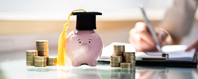 Stacked Coins And Piggy Bank With Graduation Cap In Front Of Businesswoman