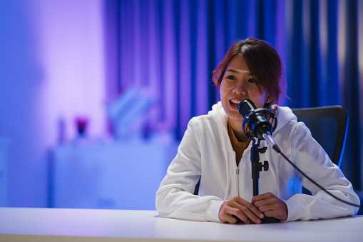 Young Asian woman recording a podcast in home studio at night. Podcaster concept.