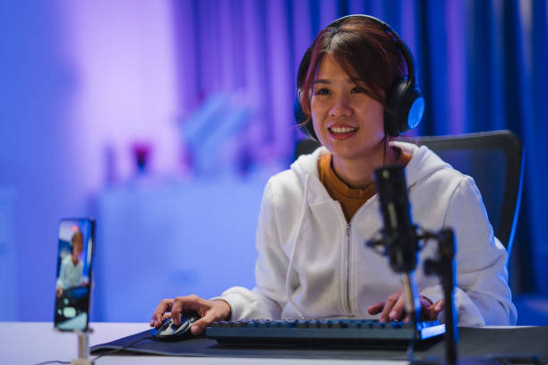istock Young Asian woman playing online computer video game and broadcast streaming live in neon lights living room at home. 1406462373