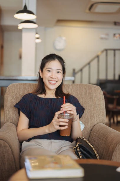 donna asiatica del college sorridente che si gode il caffè americano arancione ghiacciato nel caffè - thai cuisine asian cuisine vertical close up foto e immagini stock