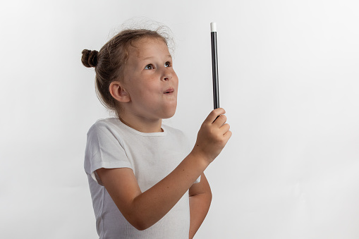 Girl magician holding up a magic wand - young magician performing with a magic wand - side view against white background