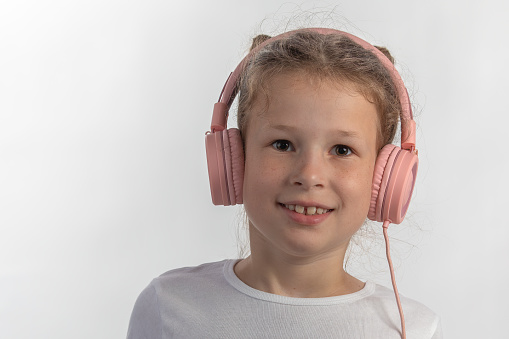 Close-up portrait of a young girl with pink headphones listening to music looking straight into camera