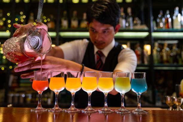 Male bartender preparing colorful cocktail drink serving to customer on bar counter at nightclub. Professional male bartender preparing colorful cocktail drink serving to customer on bar counter at nightclub. Barman making mixed alcoholic drink for celebrating holiday event party at luxury restaurant bar. bartender stock pictures, royalty-free photos & images
