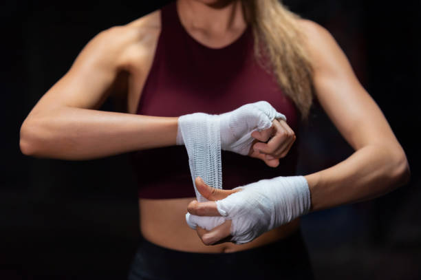 Asian woman boxer wraps her hands with boxing bandages in dark old gym Strong Asian woman athlete wraps her hands with boxing bandages while do sport training workout boxing in abandoned building. Female boxer practicing fighting exercise kickboxing in dark old gym boxercise stock pictures, royalty-free photos & images
