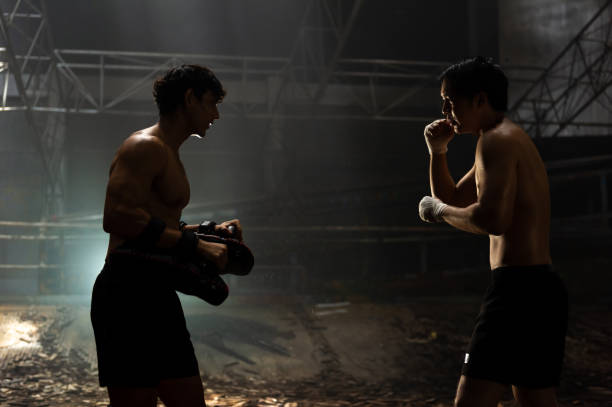 Asian man boxer do practicing boxing with male coach in abandoned building. Strong Asian sportsman practicing boxing workout punching with male combat sport trainer in abandoned building. Active man coach support male athlete boxer do fighting exercise kickboxing in dark old gym boxercise stock pictures, royalty-free photos & images