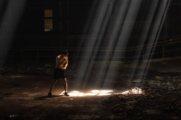 Asian man boxer practicing boxing exercise punching the air in abandoned building. Healthy and strong Asian sportsman athlete do sport training workout boxing exercise punching the air in abandoned building. Active man boxer practicing fighting exercise kickboxing in dark old gym boxercise stock pictures, royalty-free photos & images