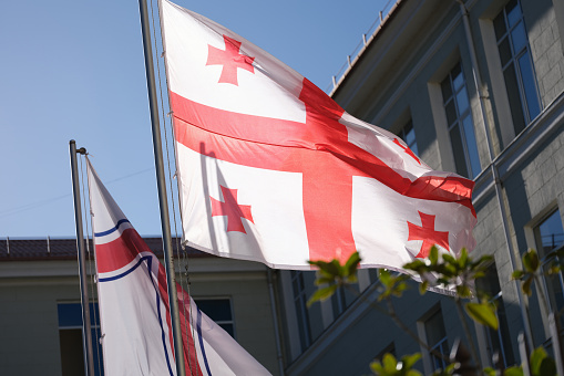 Flag of Georgia hanging near building against blue sky closeup. Georgian national symbols concept