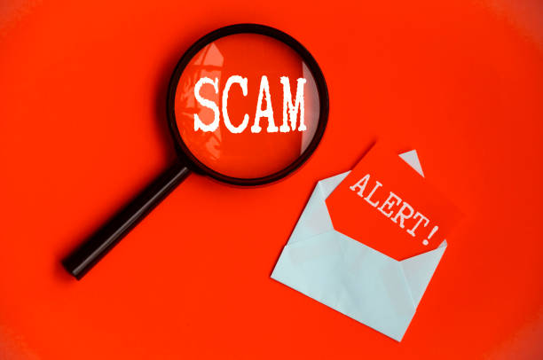 istock Scam Alert text on magnifying glass and notepad on red cover background. Scamming concept 1406471945