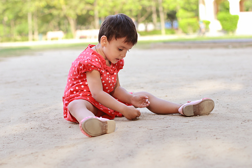 Small girl playing with soil outdoor in public park.