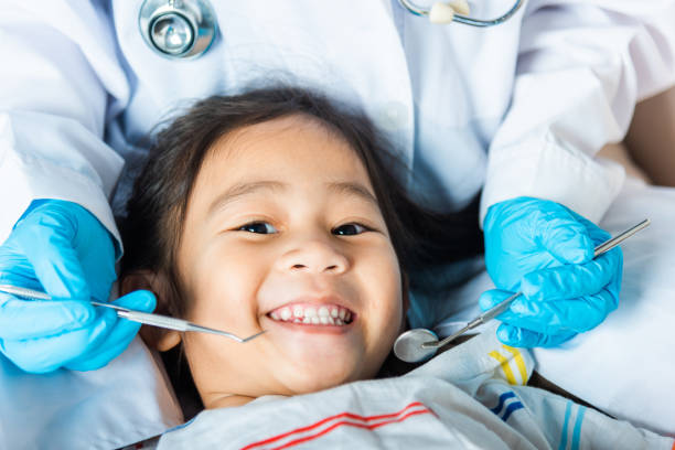 Il medico esamina la cavità orale del bambino piccolo usa lo specchio della bocca per controllare la cavità dei denti - foto stock