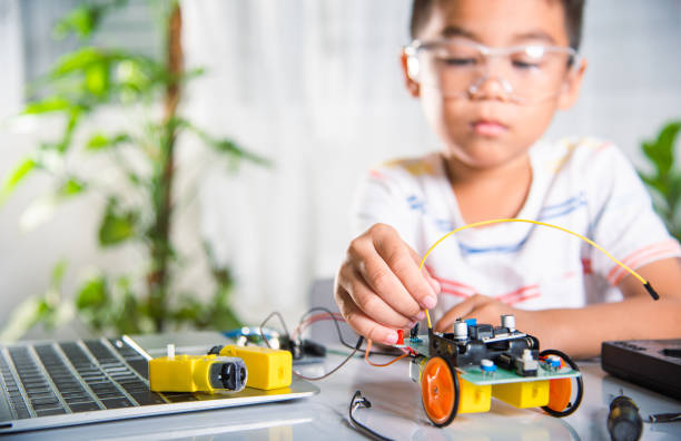 istock Asian kid boy plugging energy and signal cable to sensor chip with open-source hardware and software robot car 1406476256