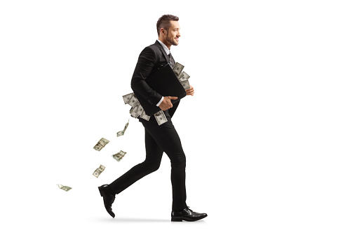 Full length profile shot of a businessman running with a briefcase full of money isolated on white background