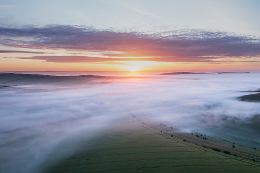 Beautiful drone landscape image of sea of fog rolling across South Downs English countryside during Spring sunrise