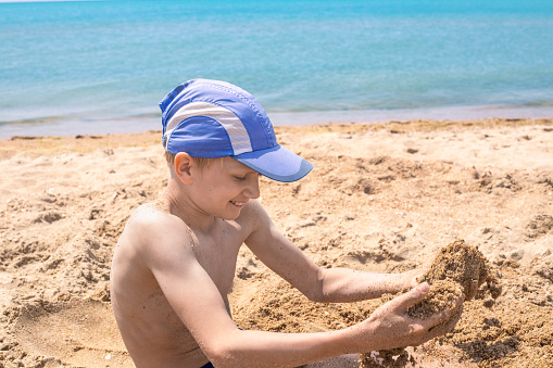 a white-haired boy plays with sand on the seashore on a summer sunny day. Happy holidays on the sea coast.