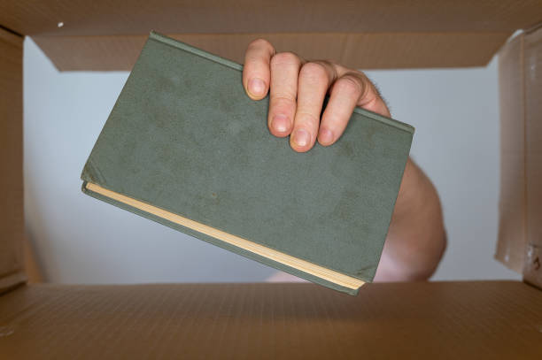istock A man's hand pulls a book out of a cardboard moving box. An old green hardcover book. Bottom view. Inside view.  Close-up. Selective focus. 1406483208