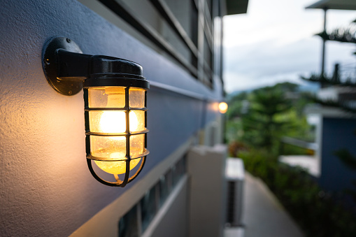 A classic style lighting bulb in metal cover is installed on building exterior wall. Electrical equipment object photo.