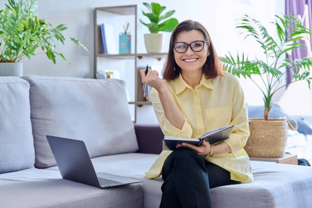 istock Mature business woman working on couch, using laptop looking at camera 1406485379