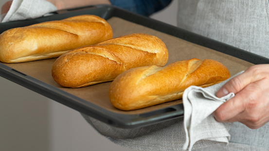 Hands hold freshly baked french baguette in baking sheet. Bread bakery. Food background