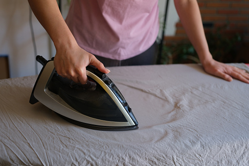 Close-up of housewife ironing wrinkled bedsheet on board using steam iron. Woman doing housework. Housekeeping and household chores concept