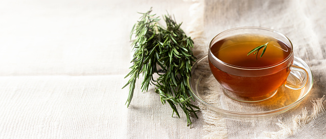 Rosemary herbal tea on linen table cloth with rosemary bunch, large image for banner with copy space. Healthy drink concept.