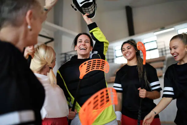 A group of young and old cheerful women, floorball team players, in gym cebrating victory.A group of young and old women, basketball team players, in gym with trophy celebrating victory.