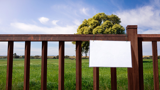 Mockup of sign on fence with oak tree and blue sky background in field countryside scenery. Layout mock up ready for your design preview. Billboard mock-up with copy space for logo design presentation
