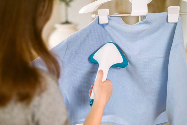 istock Using steaming iron to ironing shirt in home. Doing stream vapor iron for press clothes in hand. 1406493998