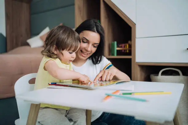 Photo of Mother and her little girl drawing together at home.