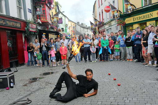 Galway, Ireland - 15 07 2013. Street Performer lies on the ground holding fire torches.\nCrowd of audience watches the show.