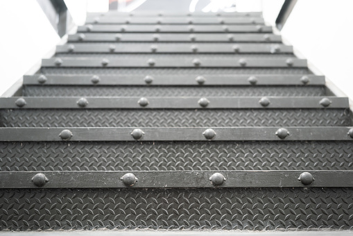 Metallic industrial designed stair step up to the higher floor, close-up and selective focus at foreground. Interior part and background photo.