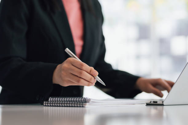 istock Close-up business woman working with laptop holding pen writing notes on notepad. 1406499071