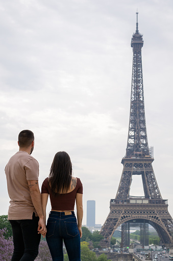 Unrecognizable couple in love in the foreground looking at the eiffel tower in the background.