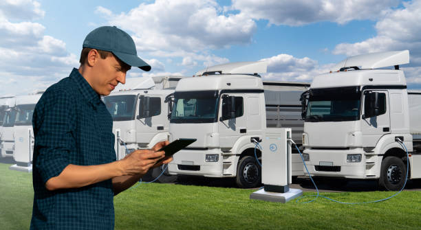 Fleet manager with a digital tablet stands next to electric trucks stock photo