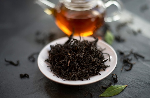 Black Tea leaves in dish on slate and glass teapot in background